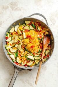 Process shot showing veggies cooking in pan.