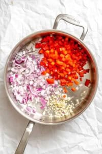 Process shot showing veggies cooking in pan.