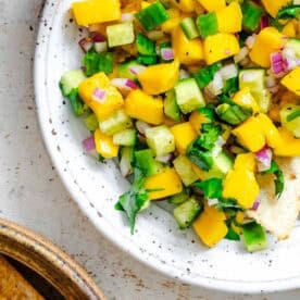 Completed Mango Cucumber Salsa on a plate against a white surface.