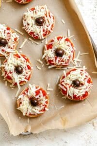 Process shots showing adding olives to mini spider pizzas.