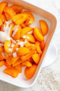Process shot showing apricots and ingredients being mixed together in a baking dish.
