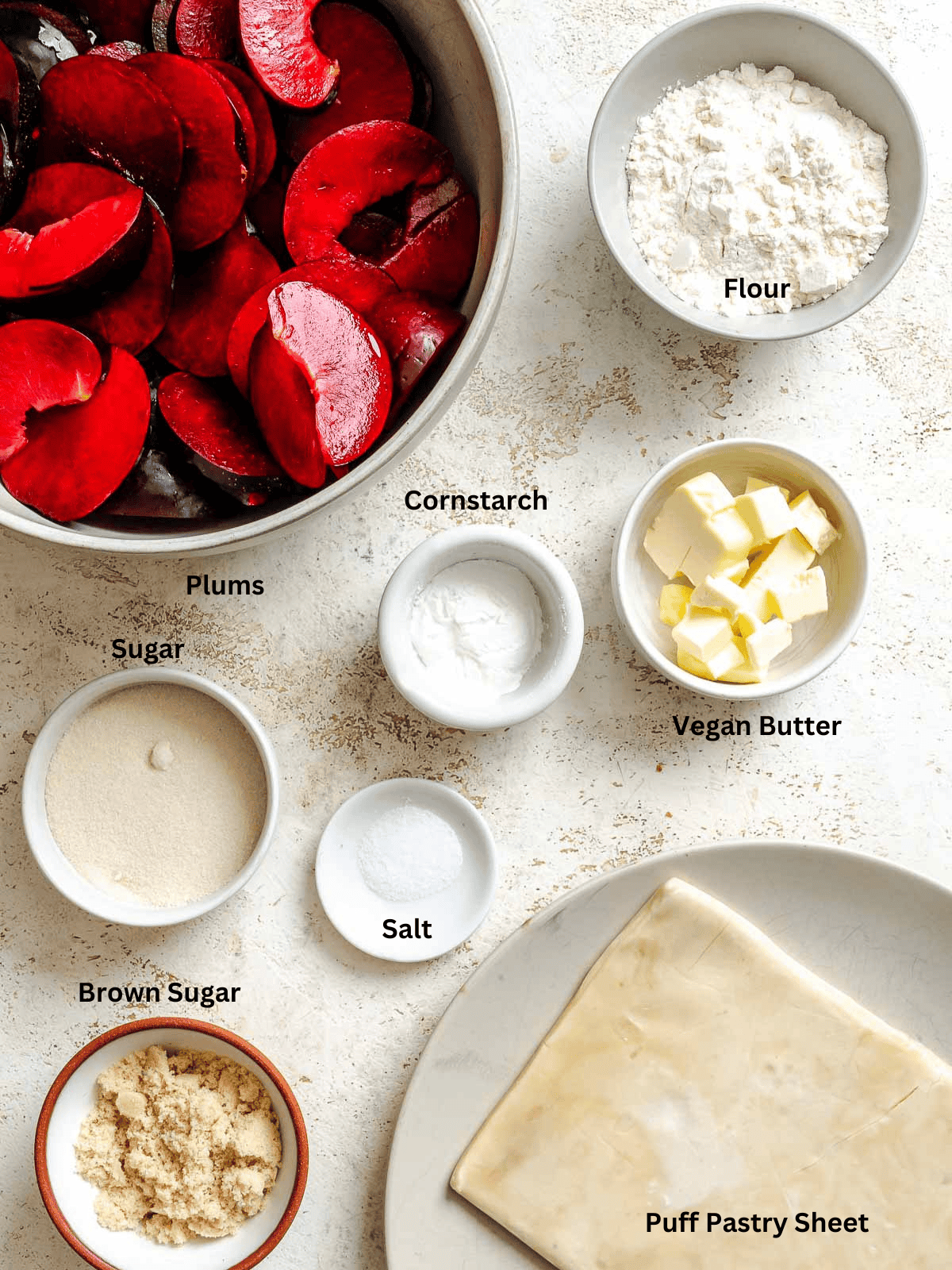 Ingredients for Easy Plum Tart (Plum Galette) measured out on a white surface.