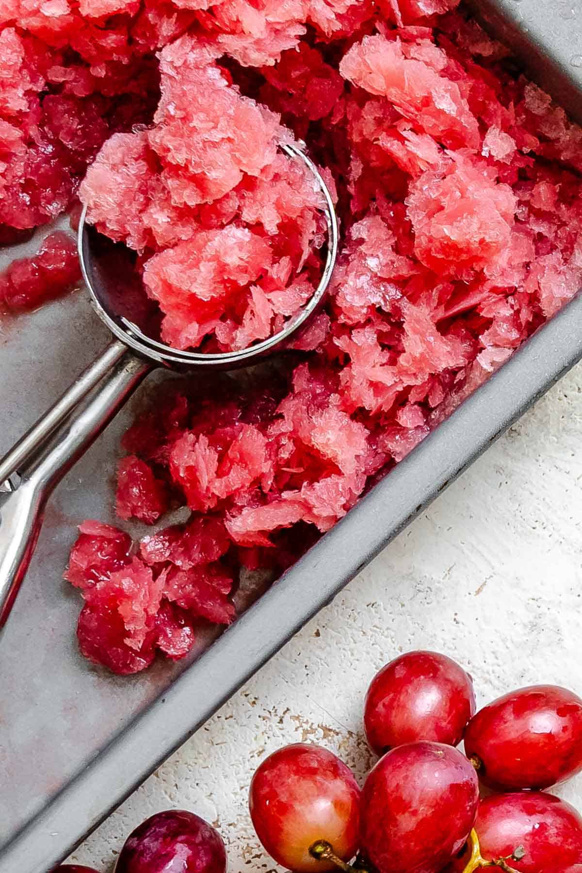 Process shot showing scooping completed Easy Grape Sorbet (Red or Green) from baking dish.