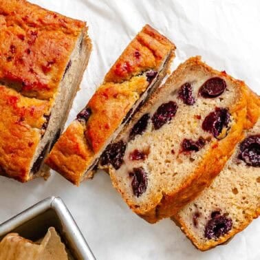 Sliced vegan cranberry orange bread with whole cranberries next to the loaf pan.