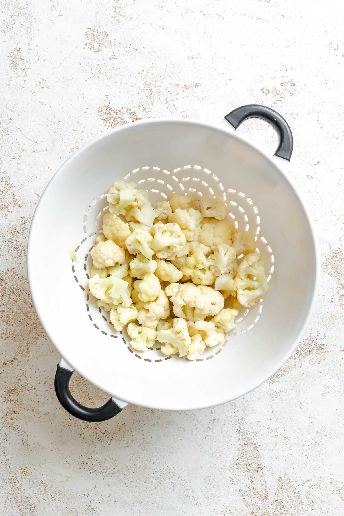 Process shot showing straining cauliflower florets in a strainer.