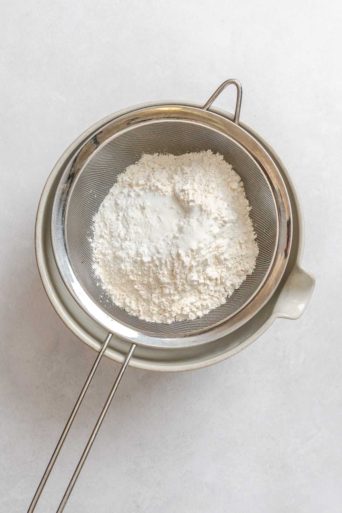 Process shot showing sifting flour into a bowl.