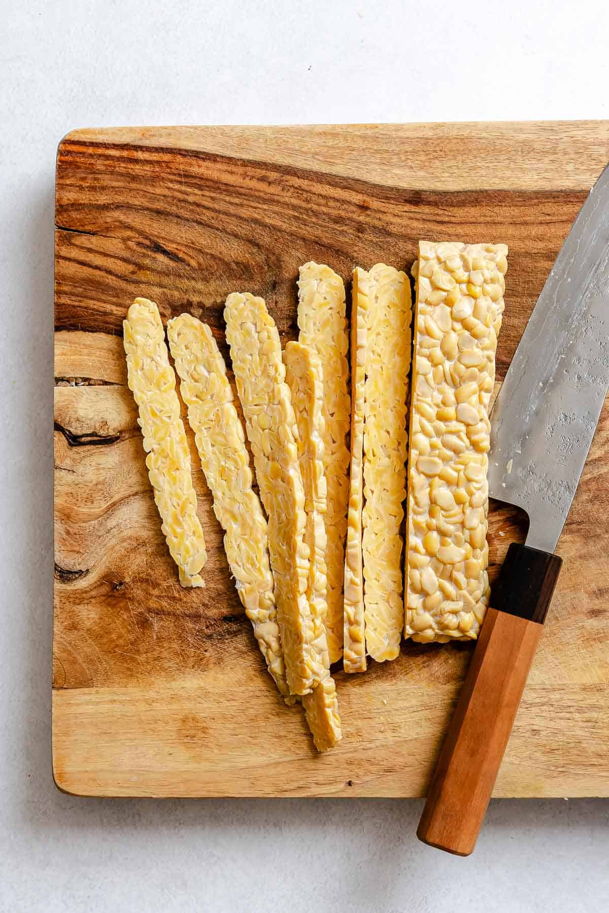 Process shot showing slicing tempeh on a cutting board.