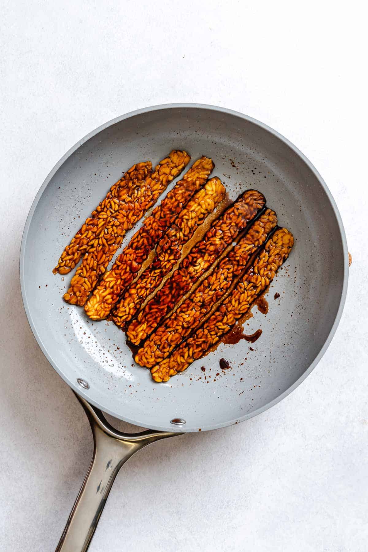 Process shot showing cooking tempeh bacon in a pan.