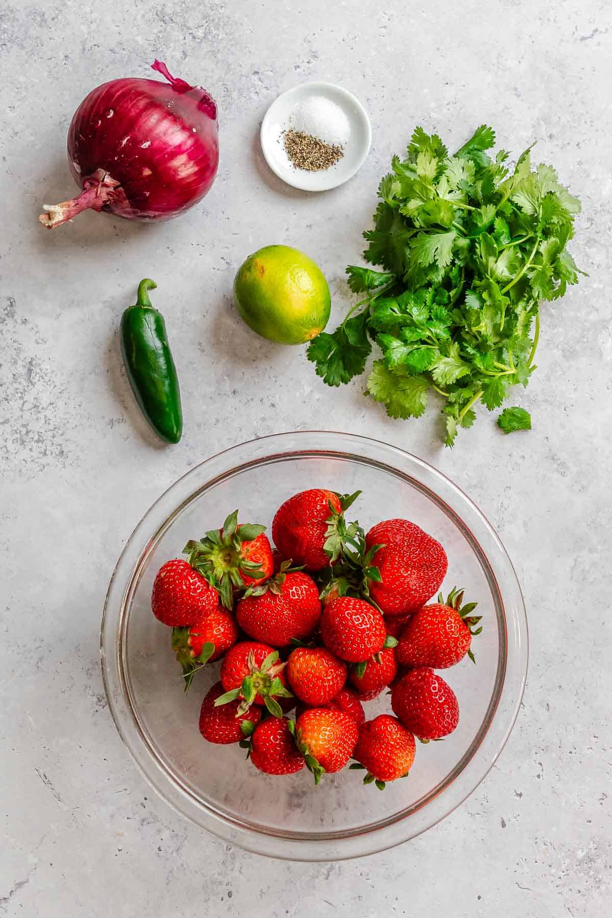 Ingredients for strawberry salsa measured out on a white surface.