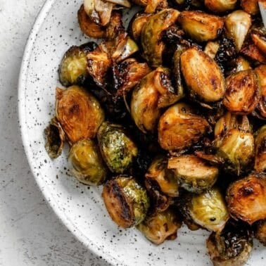 Caramelized Brussels sprouts with crispy golden edges on a white speckled plate.