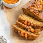Sliced vegan pumpkin bread with walnut topping on parchment paper.