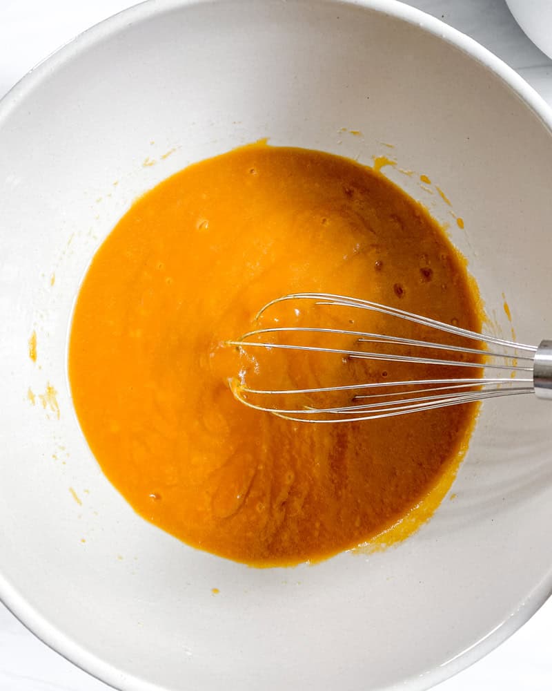 Wet ingredients for vegan pumpkin bread whisked together in a white bowl.