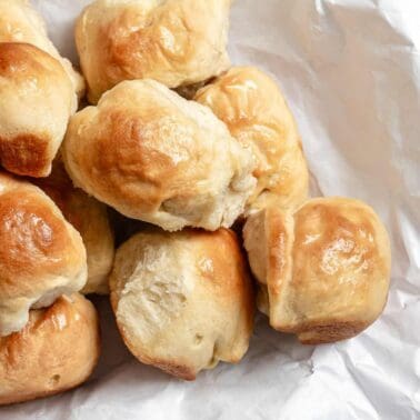 Soft, golden vegan dinner rolls brushed with melted vegan butter, piled on crinkled foil.